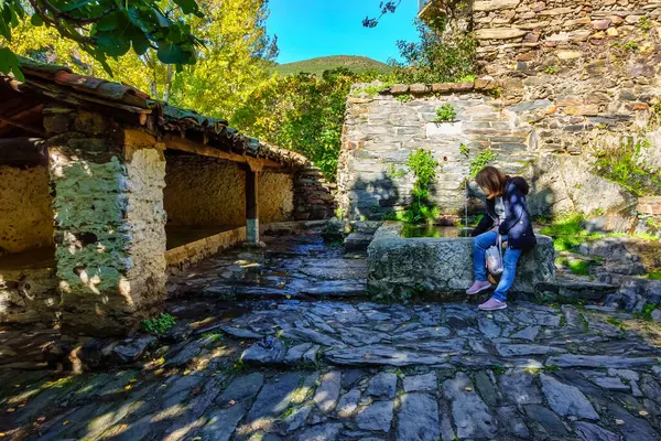 Patones de Arriba köyündeki tatlı su çeşmesinin yanında oturan turist kadın.