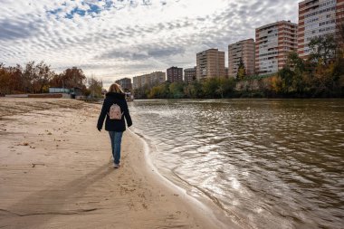 Pisuerga Nehri kıyısındaki Valladolid sahilinde sırtüstü yürüyen bir turist kadın.