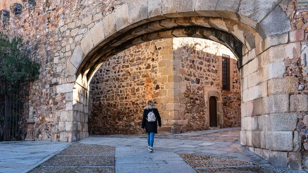 Tourist woman passing through the entrance arch in the wall that gives access to Caceres, Spain