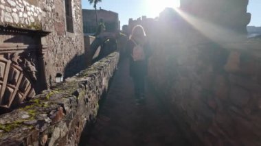 Güneş parıldarken turist kadın ortaçağ Caceres duvarında geziniyor..