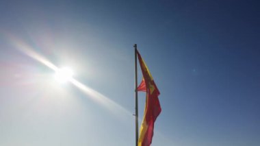 Rüzgarda sallanan İspanyol bayrağı mavi gökyüzünde parlayan güneşle ağır çekimde.