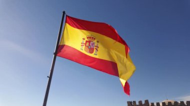 Rüzgarda dalgalanan İspanyol bayrağı, mavi gökyüzünde parlayan güneşle, Trujillo.