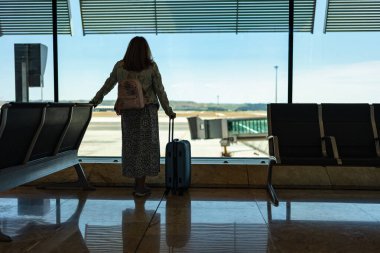 Sırtı dönük bir kadın, geciken uçuşu yakalamak için beklerken pencereden dışarı baktı.