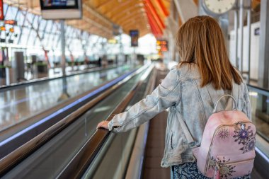 Eli yürüyen merdivende dinlenen bir kadın havaalanının uzun koridorlarında yürüyor.