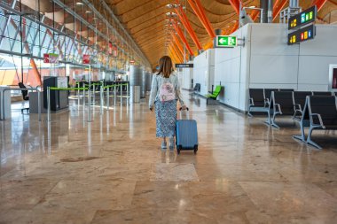 Sırtı dönük bir kadın valiziyle havaalanı koridorlarında yürüyor, Barajas, Madrid.