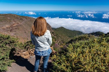 Sırtı dönük bir kadın dağın tepesinden gelen etkileyici manzarayı düşünürken, La Palma