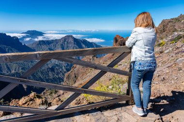 Sırtı dönük bir kadın dağın tepesinden gelen etkileyici manzarayı düşünürken, La Palma