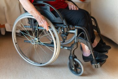 Tekerlekli sandalyesini tutan yaşlı bir kadının odanın içinde hareket etmesinin detayları.