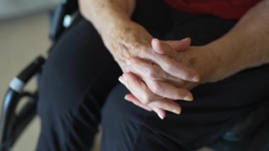 Yaşlı bir kadının elleri tekerlekli sandalyede oturuyor ve alyansını gösteriyor.