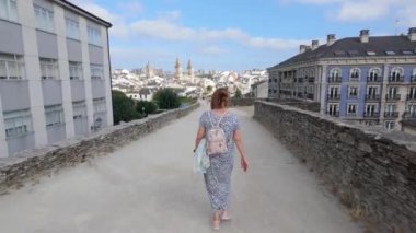 Galiçya 'nın eski Lugo kasabasını tamamen çevreleyen Roma duvarı boyunca geriye doğru yürüyen turist kadın.