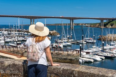 Şapkalı bir turist kadın, deniz kıyısındaki Ribadeo Körfezi manzarasını seyrediyor, Galiçya