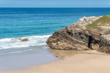 Man sitting on a chair on the beach of the cathedrals while relaxing and enjoying the sea, Galicia, Spain clipart