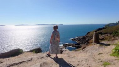 Dağın tepesinde elbise giyen ve Galiçya, Ria de Pontevedra manzarasının tadını çıkaran bir turist kadın.