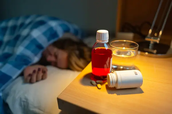 Yatakta yatan kadın grip belirtileri ve ilaç komodininin üzerinde yatıyor.