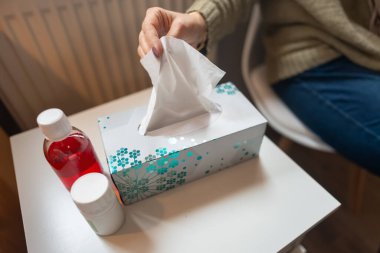 Kadınların elleri komodinin üstündeki kutudan mendil ve soğuk algınlığı ilacı alıyor.