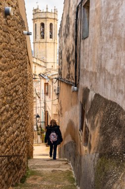 Arka planda Ortaçağ köyü kilisesi, Kretas, Teruel ile dar bir sokakta ilerleyen turist kadın.