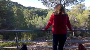 Sırtı balkona dönük bir kadın. Evinden doğanın nefes kesici manzarası.