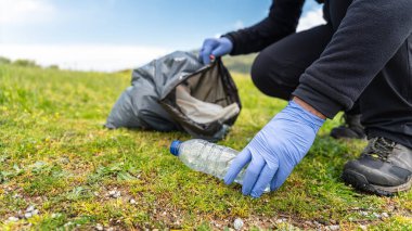 Mavi eldivenli gönüllü adam çöpleri toplayıp çöp poşetlerine atıyor.