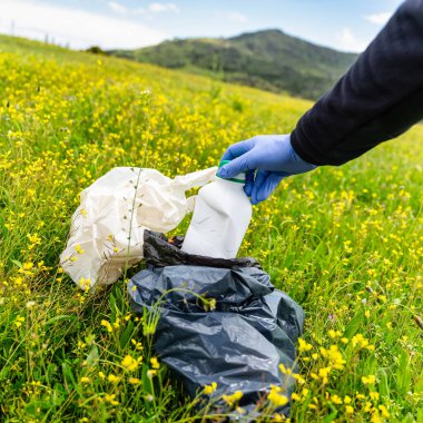 Mavi eldivenli bir adam, sorumsuz yürüyüşçülerin attığı çöpleri temizliyor.