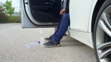Adam arabada oturuyor ve yola çöp atıyor, çevreyi kirletiyor.