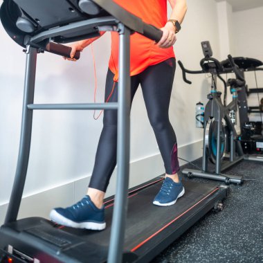 Kadın bacakları, spor salonundaki koşu bandında yelpaze açıkken yürüyor.