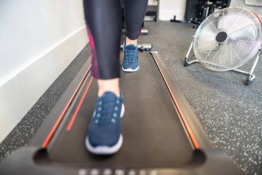 Kadın bacakları, spor salonundaki koşu bandında yelpaze açıkken yürüyor.