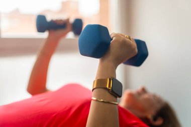 Kollarını güçlendirmek için küçük halterlerle güç egzersizleri yapan bir kadın..