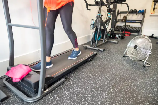 Evde spor salonunda elinde vantilatörle egzersiz yapan bir kadın.