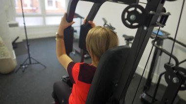 Sırtüstü yatan kadın evdeki spor makinesinde vücut geliştirme egzersizleri yapıyor.