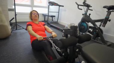 Üst düzey kadın evde ağırlık makinesiyle kürek egzersizi yapıyor.