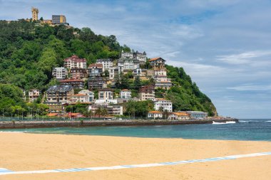 Monte Igueldo ve Ondarreta plajı güneşli bir günde altın kumuyla ön planda.