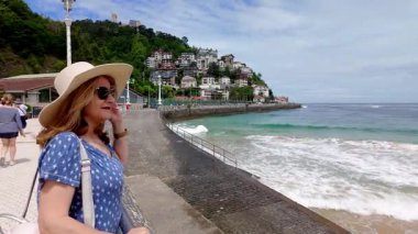 Şapkalı bir turist Donosti, Euskadi 'deki La Concha Körfezi manzarasını seyrediyor.