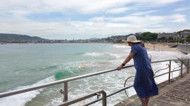 Ondarreta Sahili, San Sebastian, İspanya 'nın yanındaki deniz manzarasına bakan şapkalı ve elbiseli kadın.