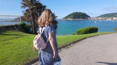 Sırtı denize dönük bir turist kadın San Sebastian, İspanya kıyılarında mavi gökyüzü ile bir günün tadını çıkarıyor.