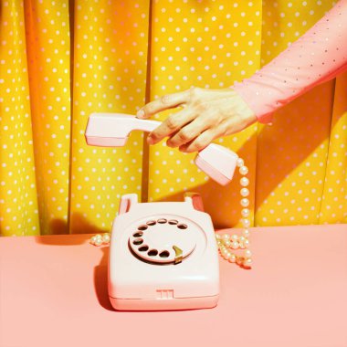 Eski moda çevirmeli telefon ve kadın eli, yaratıcı nostaljik düzen, retro estetik, pembe ve sarı arka plan. 