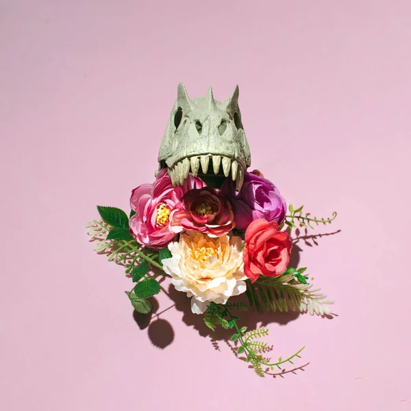 Dinozor kafatası, rengarenk çiçeklerle dekore edilmiş, Gotik esinlenilmiş çiçek deseni, pastel pembe arka plana karşı..