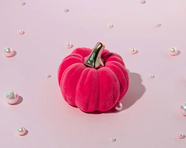 Dekoratif peluş balkabağı ve dağınık inci boncuklar, pastel pembe arka planda. Yaratıcı estetik cadılar bayramı kutlaması.