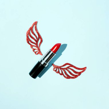 Parlak kanatlı kırmızı ruj, pastel mavi arka planda yaratıcı güzellik kompozisyonu.