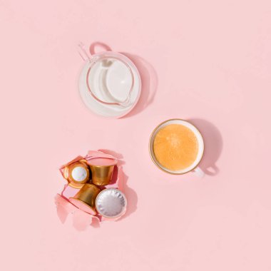 Bir fincan espresso, bir sürahi süt ve kahve kapsülü, pastel pembe arka plana karşı yaratıcı estetik tasarım. Sabah rutini..
