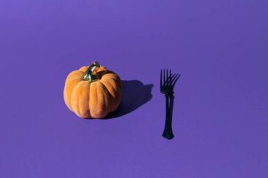 Dekoratif balkabağı ve siyah çatal, yaratıcı cadılar bayramı ilham verici mor arka plan düzeni.