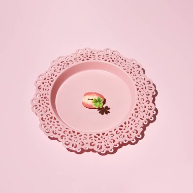 Ağzında dört yapraklı yonca, yaratıcı estetik konsept, pastel pembe arka plan. İlkbahar ilham kaynağı.