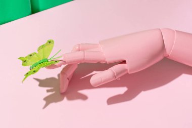 Parlak yeşil kelebek ahşap manken eline dokunuyor yaratıcı estetik düzen, pastel pembe arka plan. Bahar zamanı doğa fikri.