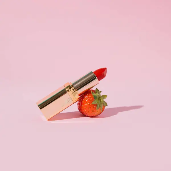 Fresh strawberry and red lipstick, creative make up layout, summer fruit flavor, pastel pink background.