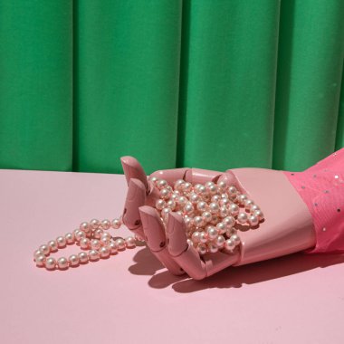 Ahşap manken eli, pastel pembe inci kolye, yaratıcı estetik retro tarzı düzen, yeşil saten kumaş arka plan..