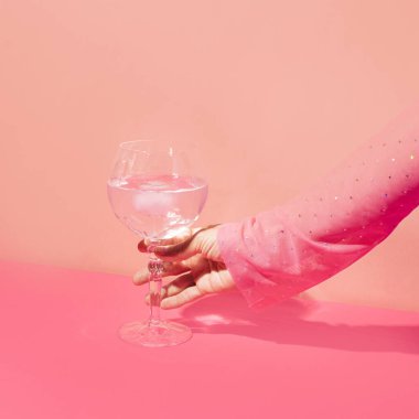 Viski bardağında pembe cin kokteyli ve parlak duvara karşı kadın eli. Kızlar parti fikri.