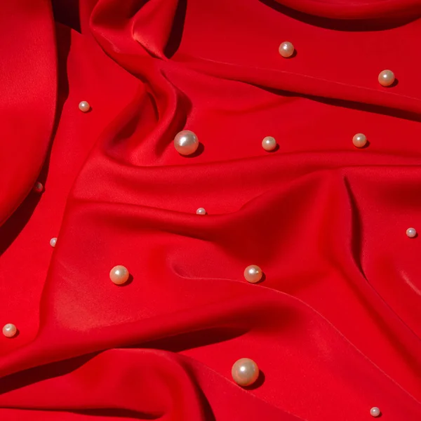 Rich red satin fabric, creative aesthetic background, pearl beads spilled.
