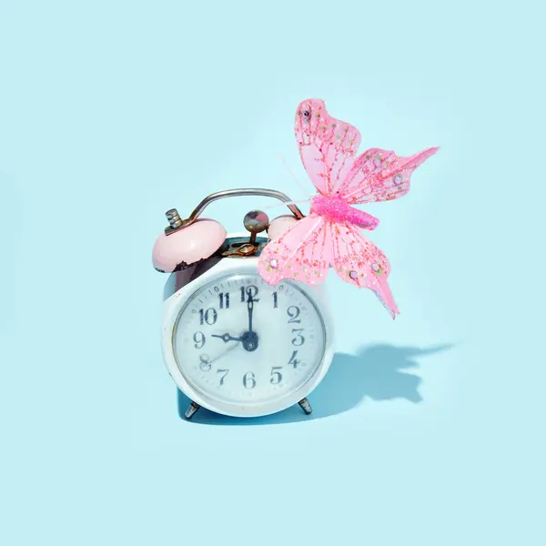 Old rusty ring bell clock, and pink decorative butterfly, creative aesthetic retro style spring inspired layout against pastel blue background.