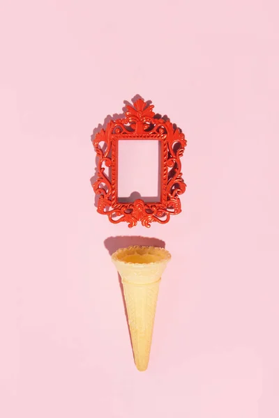 Empty picture frame and ice cream cone, creative aesthetic layout, pastel pink background.