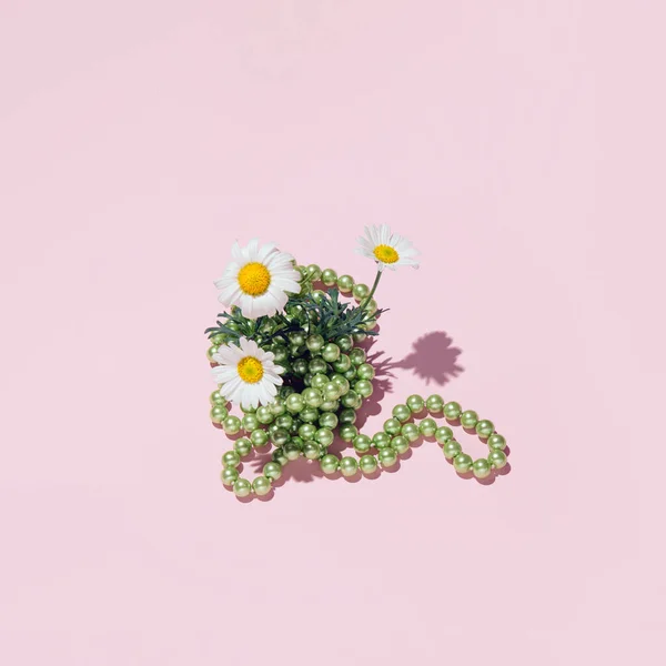 Creative aesthetic floral layout against pastel pink background. Three daisy flowers and fresh green leaves arranged with pastel green pearl beads.
