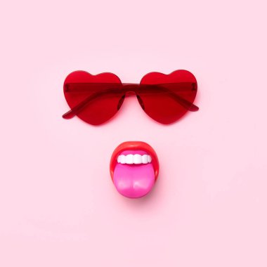 Kalp şeklinde kırmızı güneş gözlükleri, dili dışarı fırlamış, yaratıcı yaz moda tasarımları, pastel pembe arka plan.